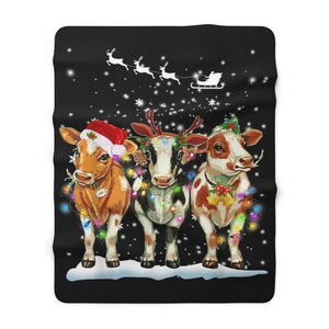Puede incluir: Tres vacas con luces de Navidad y decoraciones festivas se encuentran en una escena nevada. La vaca de la izquierda lleva un gorro de Pap&aacute; Noel, la vaca del medio lleva una diadema de cuernos de reno y la vaca de la derecha lleva una campana alrededor del cuello. Un trineo con Pap&aacute; Noel vuela en el fondo.
