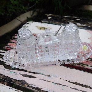 May include: A clear, cut-glass salt and pepper set with a matching sugar bowl and spoon. The set sits on a rectangular tray with a scalloped edge. The salt and pepper shakers have a dome top. The sugar bowl has a handle.
