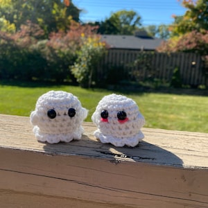 May include: Two white crocheted ghost ornaments with black eyes. One ghost has pink cheeks.