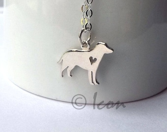 May include: A silver-colored dog pendant necklace with a heart-shaped cutout on the dog's body. The pendant hangs from a delicate chain. The necklace is displayed against a white background.