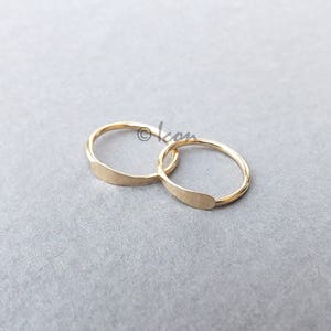 May include: Two gold hoop earrings with a flat, slightly curved design. The hoops are interlocked.