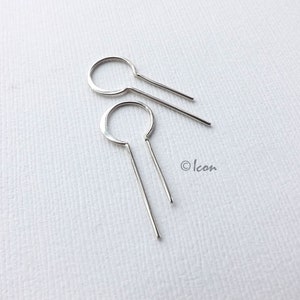 May include: A pair of silver earrings with a simple circle design and a long, thin, straight bar hanging down from each circle.