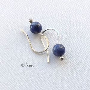 May include: A pair of silver earrings with blue gemstone beads. The earrings have a simple, elegant design.