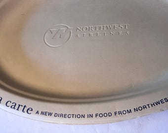 May include: Oval-shaped, beige serving tray with the Northwest Airlines logo and text. The tray features the words "a la carte" and "A NEW DIRECTION IN FOOD FROM NORTHWEST" printed on it.