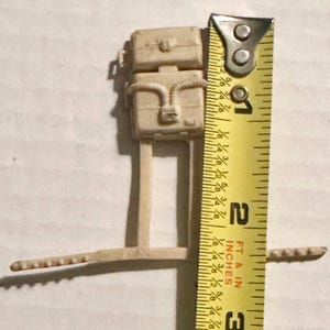 May include: A beige plastic model of a vehicle with two stacked boxes and a connecting tube. The model is approximately 1.5 inches tall, as measured by a yellow measuring tape.