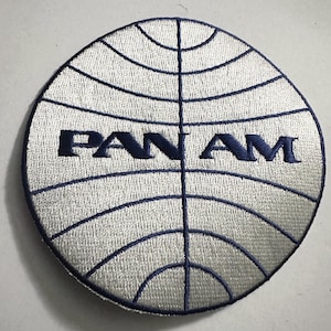 May include: A white embroidered patch with a blue globe design and the word "PAN AM" in blue lettering.