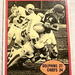 Puede incluir: Tarjeta de fútbol vintage que muestra la acción del partido de semifinales de la AFC. La tarjeta muestra jugadores con uniformes blancos y azules, con el texto "AFC SEMI-FINAL GAME" en la parte superior. El marcador es Delfines 27, Jefes 24.