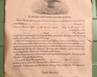 May include: A vintage document from the President of the United States of America, featuring an eagle emblem and ornate script. The document appoints Sandafo Francisco Suarez-Real as a Reserve Officer in the Navy, dated March 11, 1963. The document is aged with a yellowed paper.