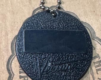 May include: Black oval-shaped keychain tag with a textured surface and a rectangular blank space. The word "Venus" is embossed on the tag. A small metal ball chain and clasp are attached at the top.