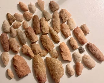 May include: A collection of various-sized, rough-hewn stones in shades of tan, beige, and reddish-brown. The stones are scattered across a white surface, showcasing their natural textures and irregular shapes. The assortment includes small, medium, and large pieces.