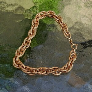 May include: A gold-toned chain bracelet featuring a series of interlocking oval links with a textured, granular surface finish. The bracelet is secured with a circular spring ring clasp, showcasing a consistent metallic luster throughout the design.