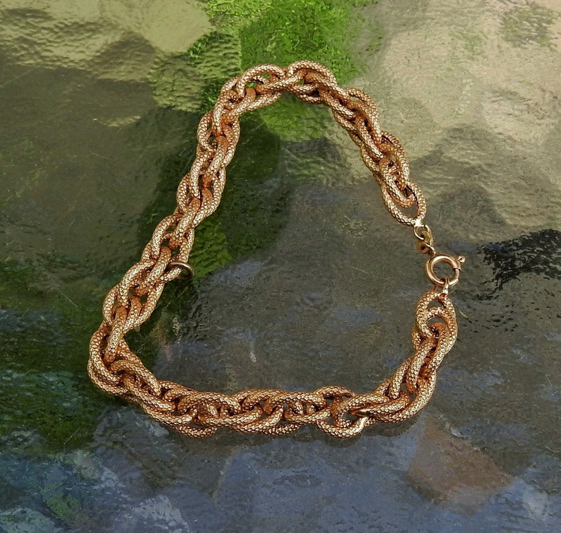 May include: A gold-toned chain bracelet featuring a series of interlocking oval links with a textured, granular surface finish. The bracelet is secured with a circular spring ring clasp, showcasing a consistent metallic luster throughout the design.