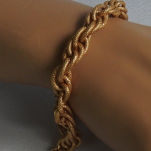 May include: A gold-toned chain bracelet featuring a series of interlocking, textured oval links. The surface of each link has a fine, granular finish that catches the light, creating a consistent metallic appearance across the entire piece of jewelry.