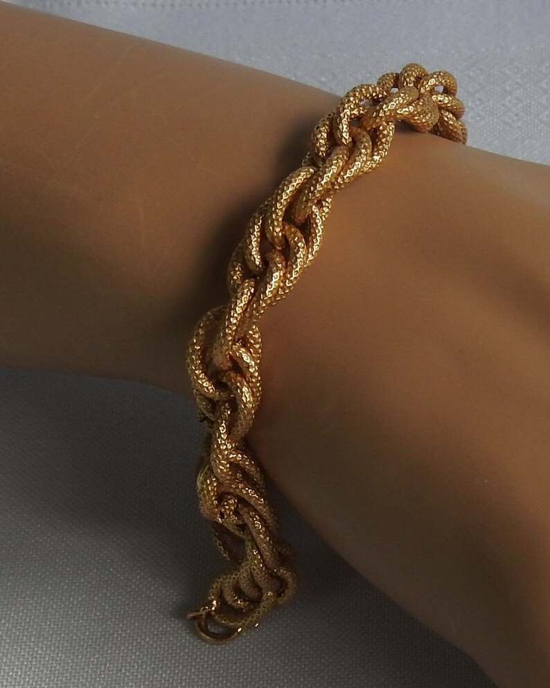 May include: A gold-toned chain bracelet featuring a series of interlocking, textured oval links. The surface of each link has a fine, granular finish that catches the light, creating a consistent metallic appearance across the entire piece of jewelry.