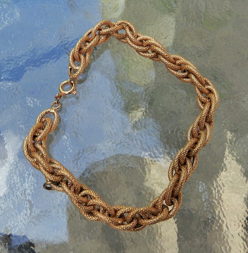 May include: A gold-toned chain bracelet featuring thick, interlocking oval links with a textured, granular surface finish. The bracelet is secured with a circular spring ring clasp, showcasing a consistent metallic appearance throughout the entire piece.