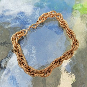 May include: A gold-toned chain bracelet featuring thick, interlocking oval links with a textured, granular surface finish. The bracelet is secured with a small, circular spring-ring clasp mechanism that connects the two ends of the chain.