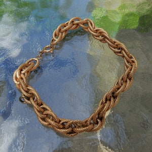 May include: A gold-toned chain bracelet featuring thick, interlocking oval links with a textured, granular surface finish. The bracelet includes a circular spring ring clasp mechanism for closure, showcasing a consistent metallic luster throughout the design.
