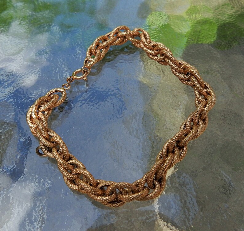 May include: A gold-toned chain bracelet featuring thick, interlocking oval links with a textured, granular surface finish. The bracelet includes a circular spring ring clasp mechanism for closure, showcasing a consistent metallic luster throughout the design.