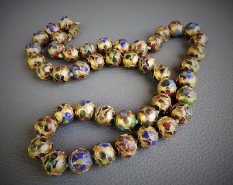 May include: A necklace featuring gold-toned, round beads with colorful floral enamel designs in red, blue, green, and yellow. The beads are strung together, creating a decorative jewelry piece.