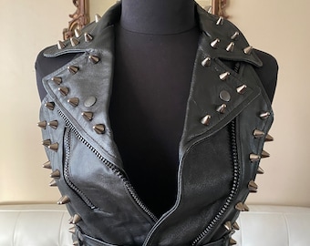 May include: A black leather vest with a zipper closure and a belt. The vest is decorated with silver studs.
