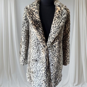 May include: A long-sleeved coat featuring a faux fur texture with a prominent leopard print pattern in shades of black, gray, and tan. The garment includes a wide notched lapel collar and a straight-cut silhouette that falls to the mid-thigh.