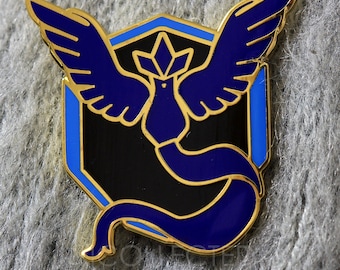 May include: Gold-colored enamel pin featuring a blue bird with a black body and wings, surrounded by a blue and gold hexagonal frame. The bird is depicted with a stylized wing design and a blue tail.