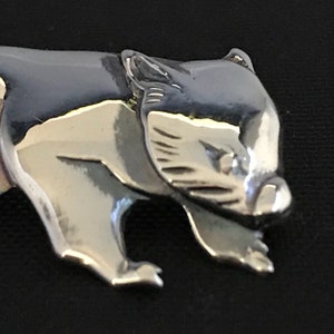 Op de afbeelding: Een zilverkleurige metalen bedel in de vorm van een lopende wombat. De bedel is gedetailleerd met een textuur van bont en een realistisch gezicht.