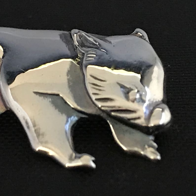 Op de afbeelding: Een zilverkleurige metalen bedel in de vorm van een lopende wombat. De bedel is gedetailleerd met een textuur van bont en een realistisch gezicht.