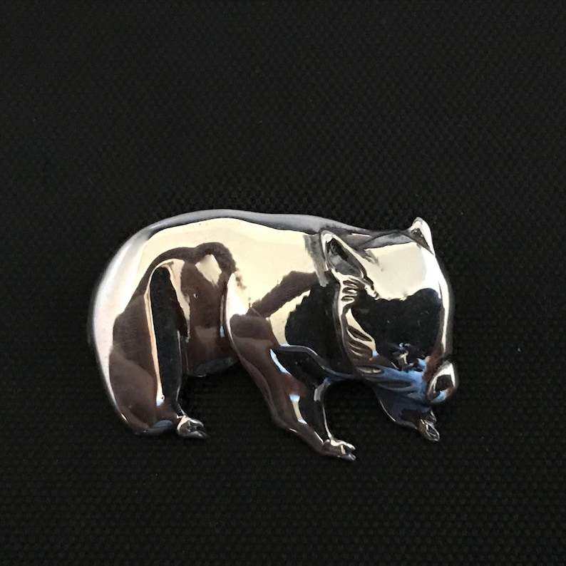 Op de afbeelding: Een driedimensionale, zilverkleurige broche van een wombat. De wombat is afgebeeld in een wandelende houding met zijn hoofd naar beneden.
