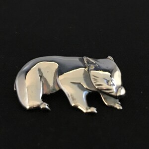 Op de afbeelding: Een zilverkleurige broche in de vorm van een wombat. De wombat is afgebeeld in een wandelende houding met zijn hoofd naar de zijkant gedraaid.