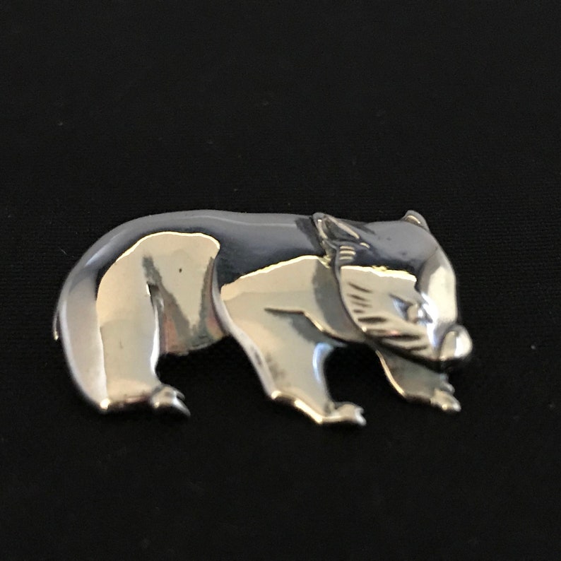 Op de afbeelding: Een zilverkleurige broche in de vorm van een wombat. De wombat is afgebeeld in een wandelende houding met zijn hoofd naar de zijkant gedraaid.