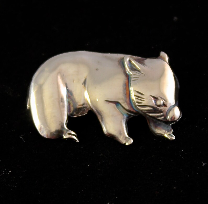 Op de afbeelding: Een zilverkleurige broche in de vorm van een wombat. De wombat wordt afgebeeld in een wandelende houding, met zijn kop naar de zijkant gedraaid. De broche is gedetailleerd met een getextureerd oppervlak en een realistische weergave van de kenmerken van de wombat.