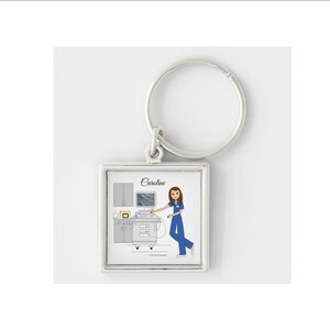 May include: A silver keychain with a square-shaped charm featuring a cartoon illustration of a person in a blue uniform operating an ultrasound machine. The charm has the name "Caroline" printed on it.