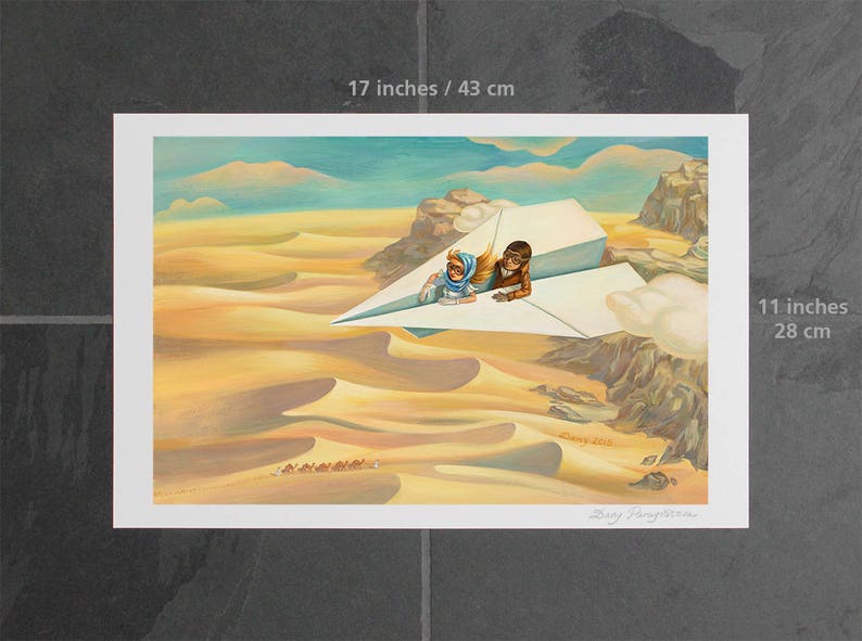 May include: A framed art print, 17 x 11 inches, depicts two figures riding a paper airplane over a desert landscape. The artwork features warm tones of yellow and brown, with a blue sky and clouds. A caravan of camels is visible in the distance.