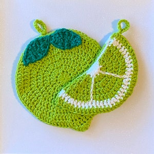 May include: Two crocheted lime-shaped pot holders. One is a whole lime with green leaves and the other is a lime wedge with white stitching.