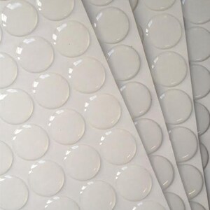 May include: A sheet of white adhesive-backed clear round stickers. The stickers are arranged in rows and columns on a white sheet.
