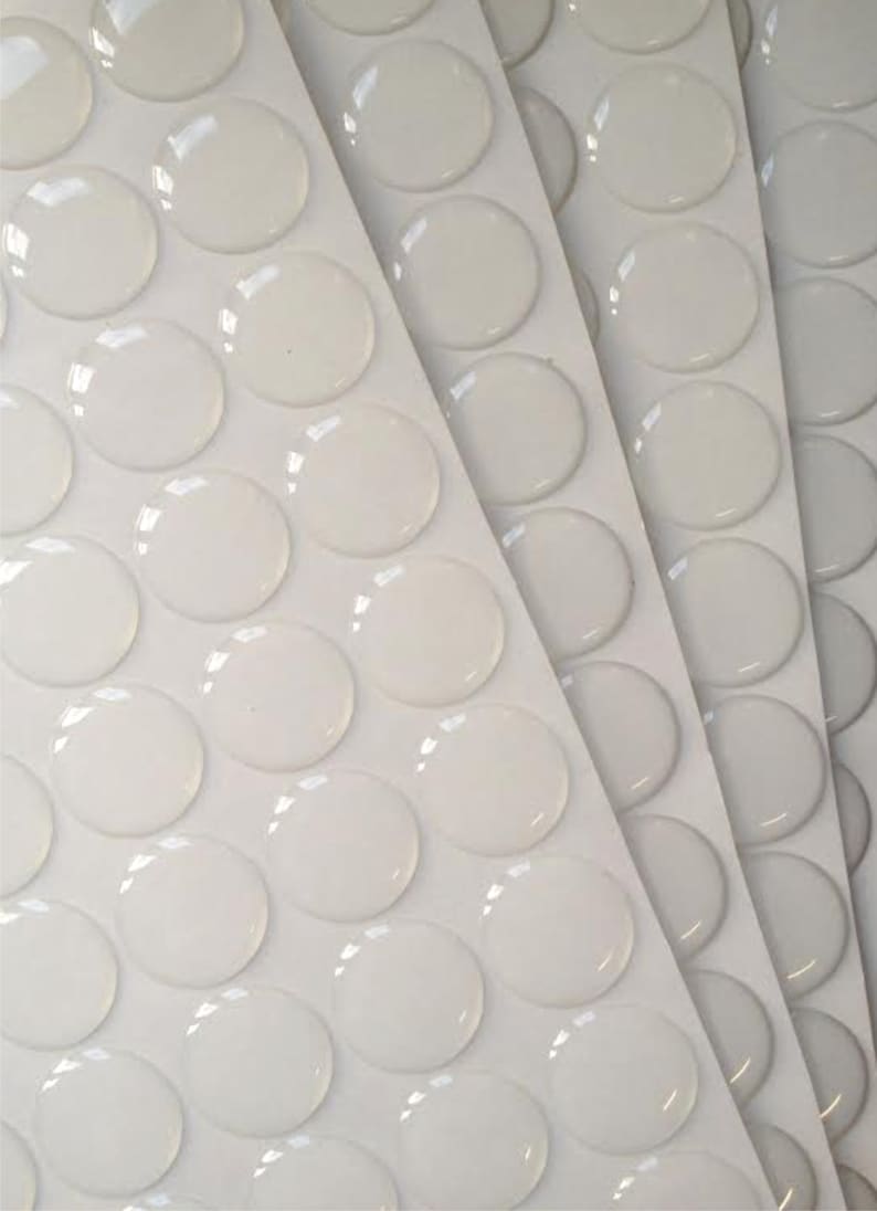May include: A sheet of white adhesive-backed clear round stickers. The stickers are arranged in rows and columns on a white sheet.