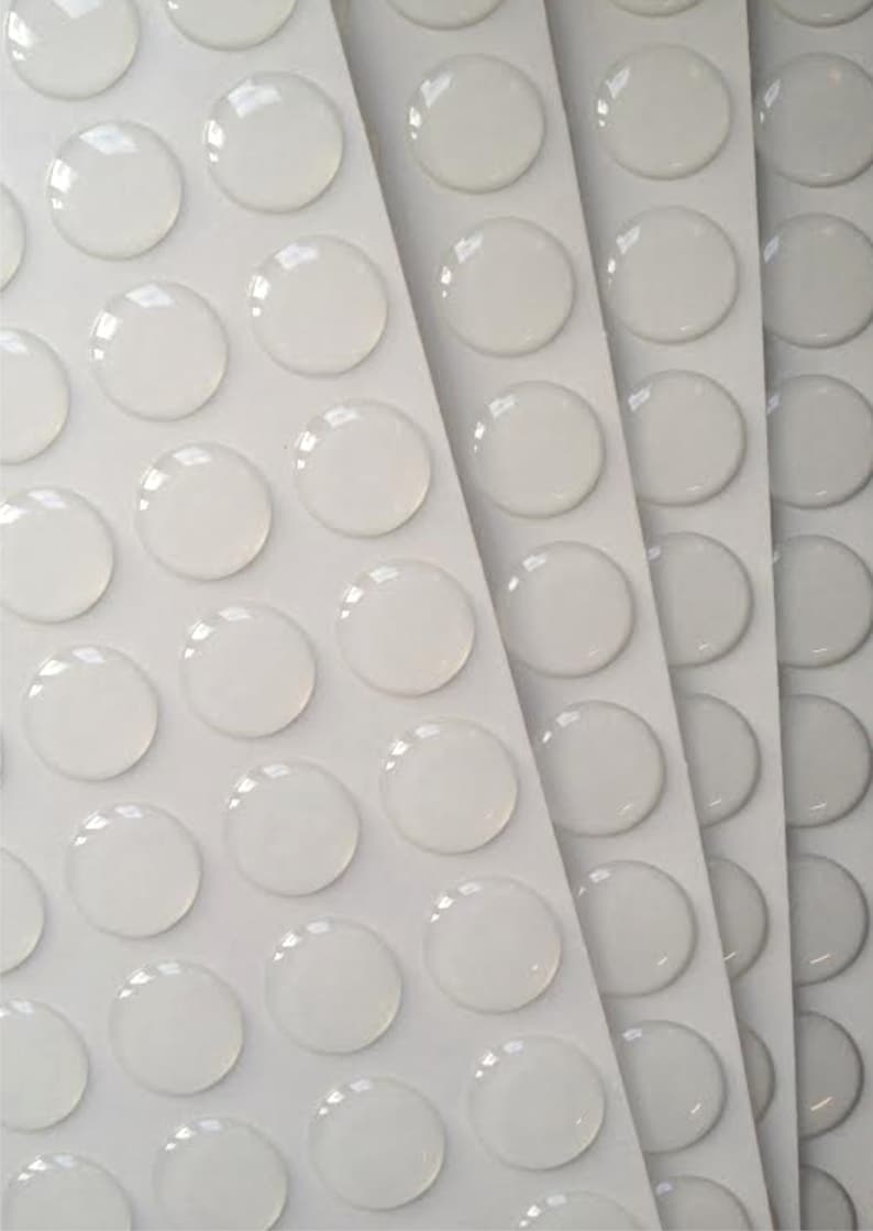 May include: A sheet of clear adhesive dots, arranged in rows on a white background.