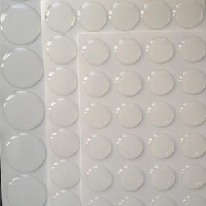 May include: A sheet of clear adhesive dots, arranged in rows and columns on a white background. The dots are round and translucent, with a slight sheen.