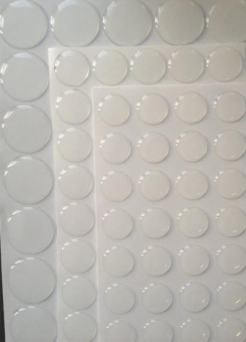 May include: A sheet of clear adhesive dots, arranged in rows and columns on a white background. The dots are round and translucent, with a slight sheen.