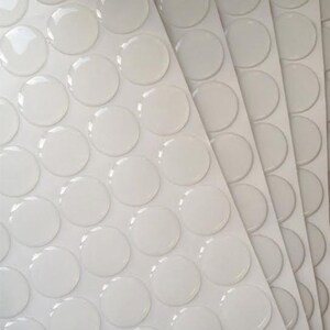 May include: A sheet of clear, round adhesive stickers on a white background. The stickers are arranged in rows and columns.