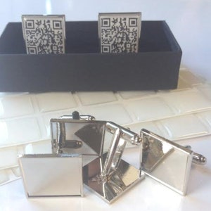 Könnte beinhalten: Ein Satz silberner Manschettenknöpfe mit quadratischem Design. Zwei der Manschettenknöpfe haben ein schwarz-weißes QR-Code-Design. Die anderen beiden Manschettenknöpfe sind schlicht silber.