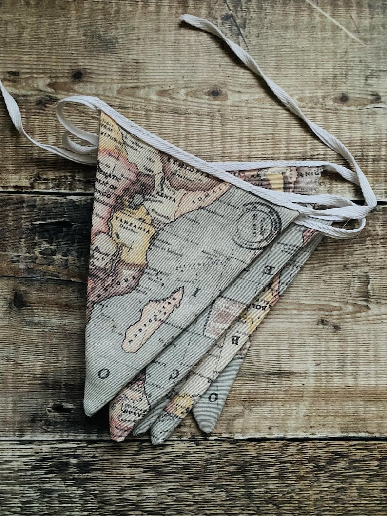 May include: A set of fabric pennants with a vintage world map design. The pennants are beige with brown, yellow, and red accents. The map features the continents of Africa and Australia. The pennants are strung together with white string.