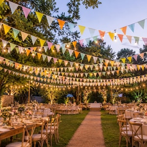 Puede incluir: Escenario de evento al aire libre con mesas, sillas y centros de mesa florales. Banderas triangulares de colores y guirnaldas de luces están suspendidas en lo alto, creando un ambiente festivo. La escena se desarrolla en una zona de césped con árboles al fondo.