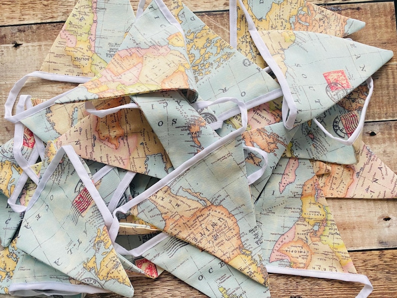 May include: A set of blue and beige fabric pennants with a vintage world map design. Each pennant has a white trim and is strung together with white string.
