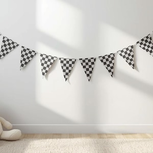 Op de afbeelding: Een zwart-wit geblokte vlaggenbanner hangt aan een witte muur. De kamer heeft een neutraal kleurenpalet met een beige tapijt, een houten bed, een teddybeer, een rieten mand en kleurrijke blokken.