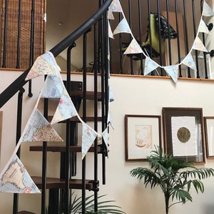 May include: A white and blue map-themed banner hangs on a black metal staircase railing. The banner is made of fabric and has a scalloped edge. The banner is decorated with a map of the world. The banner is hanging on a staircase railing in a home.