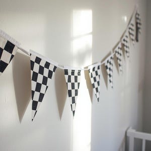 May include: A garland of black and white checkered flags hangs on a wall. The pennants are triangular and made of fabric. The flags are strung together on a white string, creating a racing theme.