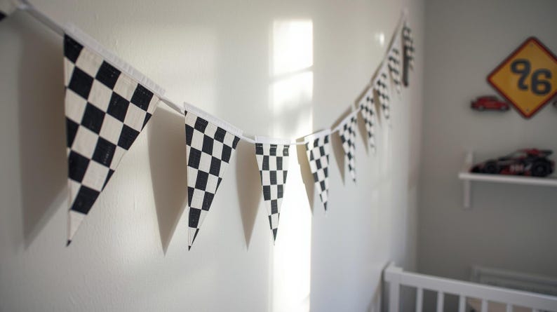 May include: A garland of black and white checkered flags hangs on a wall. The pennants are triangular and made of fabric. The flags are strung together on a white string, creating a racing theme.