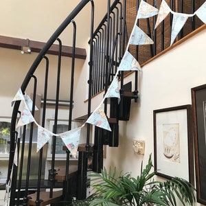 May include: A white and blue map-themed bunting hangs on a black metal spiral staircase. The bunting is strung between the railing and the wall. A green plant is in the foreground.